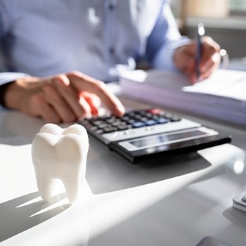Someone calculating cost with binder, pen, calculator at desk with model tooth