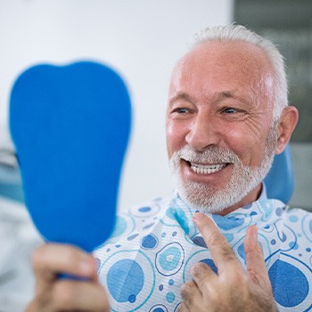 Man smiling while looking at reflection in handheld mirror