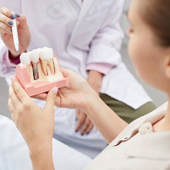 Dentist pointing to model dental implant held by patient